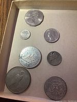 Photo showing seven coins arranged in a box, including a large Australian 50 cent coin, US Kennedy half dollar, and other US coins.