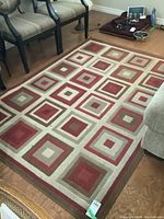Full view of the rectangular area rug on wood floor with geometric square pattern in shades of red, beige, and brown.