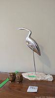 Photo of metal flamingo sculpture mounted on a stone base with two small brass owls beside it.