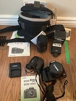 Overview of lot: open soft camera bag, Canon Rebel XS body with strap, EF 55-250mm lens, Braun Hobby flash, Minolta binoculars, battery charger, manuals
