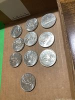 10 Canadian silver dollar coins arranged in a cardboard box, showing the reverse side featuring canoe and inscriptions.