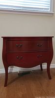 Front view of red-stained Bombay style chest of drawers with two drawers and metal pulls.