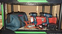 Full view of the Bosch drills, Black & Decker drill, Bosch bag, red toolbox, charger and cables on black shelving unit.
