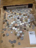 Photo displaying an assortment of multiple coins laid out in a shallow cardboard box, showcasing diversity in size, color, and wear.