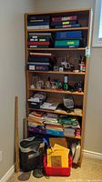 Full view of shelving unit containing binders, office supplies, calculator, paper shredder and desk lamp, organizer trays on bottom shelves