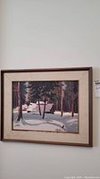 Framed painting with beige mat showing winter log cabin in snow with trees around.