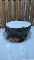 Planter shown outside in backyard covered with snow, showing overall size and round form.