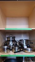 Photo of the full assortment of various stainless steel pots and pans with lids on a shelf.