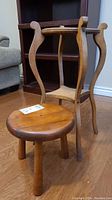 Two wooden furniture items: small stool and vintage plant stand. Stool is round with three legs, stained top. Plant stand has carved curved legs.