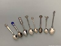 Eight assorted 925 silver collectors spoons arranged side by side, showing various decorative handles and bowl shapes.