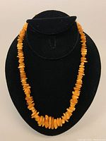 Full view of the amber bead necklace displayed on black velvet stand, showing the graduated bead sizing and warm honey-orange color.