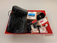 Overview photo showing Logitech speakers, Canon power winder units, Kodak lens, Epson ink cartridges, assorted optical filters in a red bin