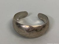 Angled view showing the textured etched pattern on the surface of the silver cuff bangle with its curved form and open-ended style.