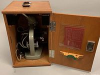 Closed wooden case with handle, opened showing microscope inside and key attached to the door.