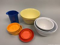 Overall lot view showing a variety of melamine bowls in cream, white, orange, yellow and a blue pitcher.