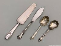 Four sterling silver handled serving utensils displayed side by side: pie cutter, spreader, two spoons.