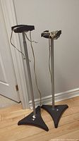 Two full metal speaker stands leaning against a wall showing adjustable height and wires attached to top platform