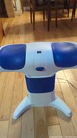Front and top view of the massager showing its blue cushioned pads and white body on a hardwood floor.