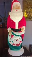 Front view of the vintage blown mold Santa Claus figurine, showing painted red suit, white beard, green sack with toys, and black belt.
