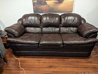 Front view of the brown leather couch showing the three padded seat cushions and three back cushions with rounded armrests.