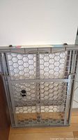 Front view of the gray expandable safety gate with honeycomb grid design.