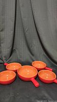 Five red terracotta terracotta soup bowls with glazed interior, four smaller and one larger with handles, on black fabric background