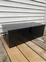 Full view of black lockable metal utility box on a wooden surface, showing diamond plate texture and one side handle.
