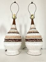 Pair of mid-century ceramic atomic table lamps standing side by side on a flat surface showing their full height and texture.