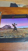Front view of the Pink Floyd album cover showing a couple dancing in front of a farmhouse at sunset with Pink Floyd branding and album title.