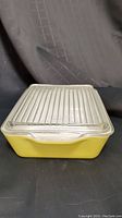 Yellow Pyrex rectangular refrigerator dish with clear ribbed lid, front view showing handles and dish shape.