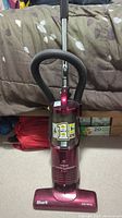 Full upright view of red Shark vacuum cleaner with flexible hose, metal wand and dust bin.
