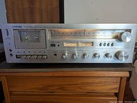 Front view of Toshiba TMC-7560 receiver showing cassette deck, tuner dial, control knobs and meters.