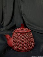 Side view showing red cast iron teapot with bamboo basket weave pattern on body and lid, black handle and spout tip.