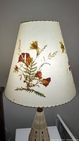 Front view of vintage Dornbusch pressed leaf lamp shade showing botanical pressed leaf and flower designs on translucent cream material.