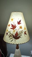 Front view of conical lamp shade showcasing pressed leaves and flowers embedded in a translucent material, illuminated from inside.