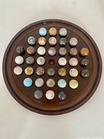 Top-down photo showing 36 natural marble marbles arranged on a circular wooden board with a central hole, marbles of various earth tones and blue shades.