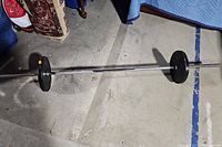 Barbell lying on concrete floor with black weight plates on each end.
