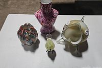 View of all four blown glass art pieces including pumpkin, bird, torso and fish on white surface in natural light