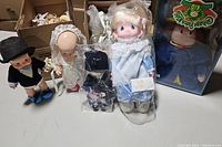 Photo of assorted dolls including boy doll, baby doll, wrapped blonde doll, small wrapped doll, and boxed Cabbage Patch Kid.