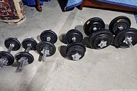 Full view of assortment of six adjustable dumbbells with black weight plates and chrome star-lock collars arranged on concrete floor.
