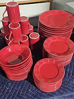 Full set of red china plates stacked, red mugs arranged in a cluster.