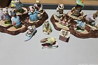Photo showing 18 Beatrix Potter porcelain figurines in various poses and costumes, arranged on two bases that mimic wooden surfaces.