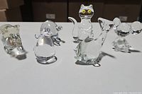 Six clear glass animal figurines (two pigs, one cat, two mice, one dolphin) displayed together on a surface.