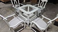 Set of square glass top table and 4 white wooden chairs with checkerboard fabric upholstery.