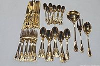 Photo showing knives, forks, teaspoons, and tablespoons arranged on a flat surface with ornate gold tone handles.