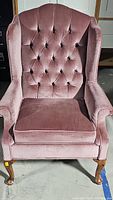 Front view of mauve velvet wingback chair with tufted back and removable seat cushion.