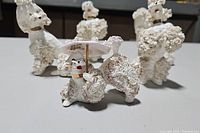Five porcelain poodles with detailed textured fur and one holding parasol