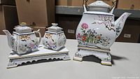 Full set including teapot, sugar container, creamer, and tray all decorated with matching floral patterns and gold accents.