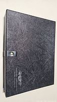 Closed black textured case with snap button closure, showing minimal wear.