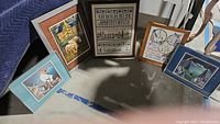 Overview of all five framed art pieces positioned on floor showing embroidery samplers and nature/animal prints.